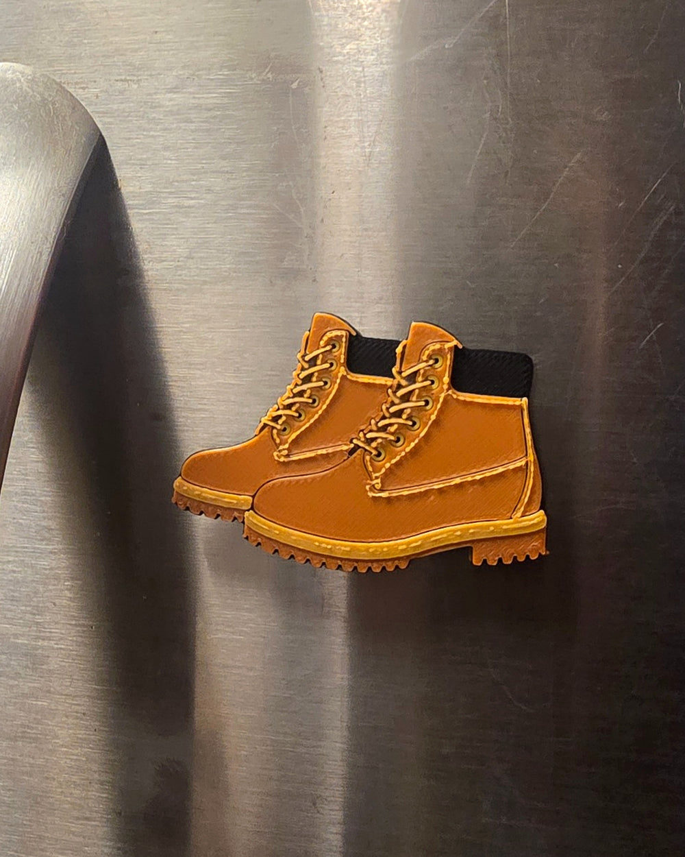 Vertical lifestyle photo of Boots 3D printed refrigerator magnet on stainless steel